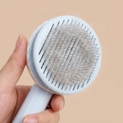 Hand holding pastel blue self-cleaning slicker brush loaded with grey cat fur