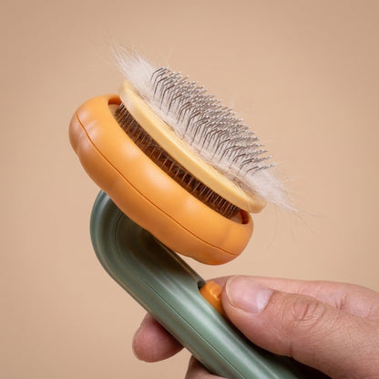 Hand pressing orange self-clean button to push fur off pumpkin cat brush