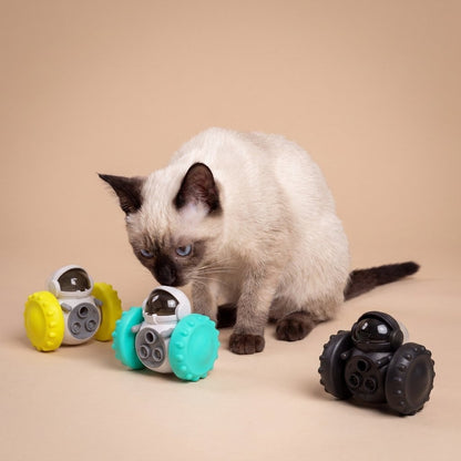 Siamese cat with yellow, teal, and black robot treat dispenser toys on tan background