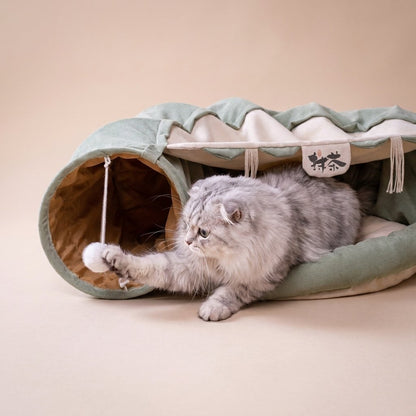 Grey tabby batting white pom-pom toy inside sage green cat tunnel bed